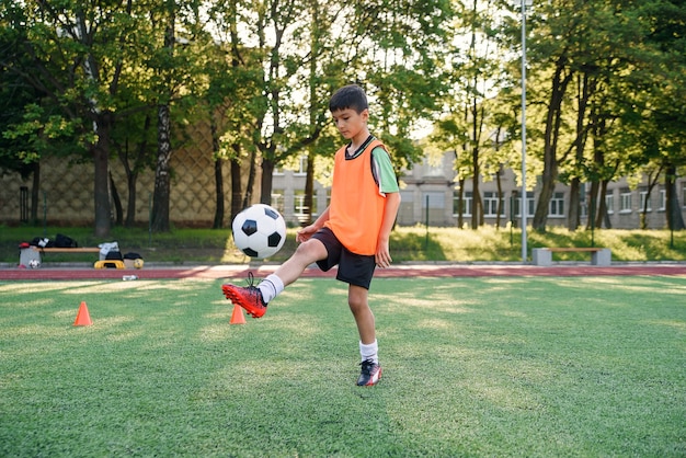 Jugador de fútbol adolescente motivado rellena el balón de fútbol en la pierna. Practicando ejercicios deportivos en artificial