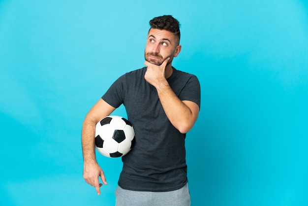 Jugador de fútbol aislado en la pared azul y mirando hacia arriba