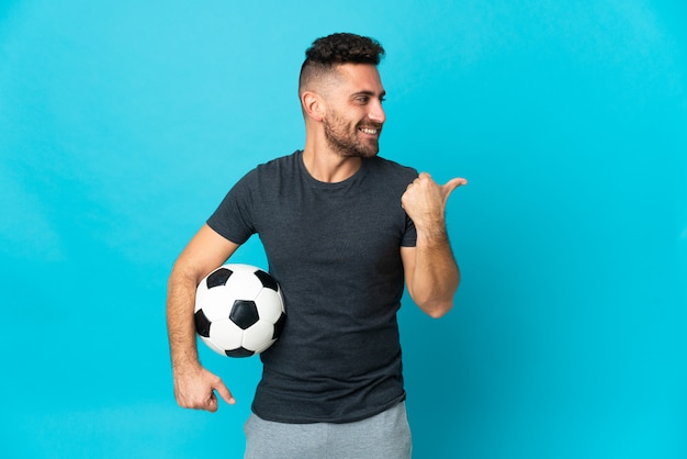 Jugador de fútbol aislado sobre fondo azul apuntando hacia el lado para presentar un producto