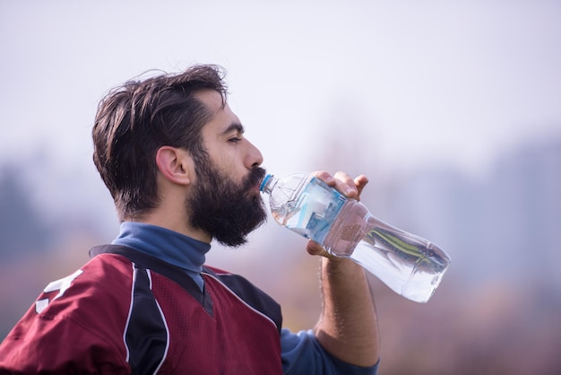 Un jugador de fútbol americano cansado bebiendo agua mientras descansa después de un duro entrenamiento en el campo