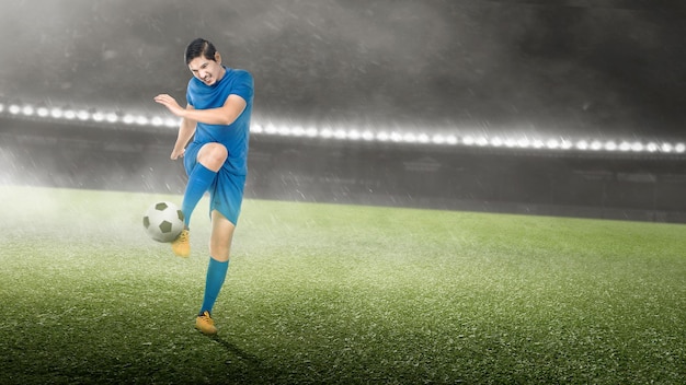 Jugador de fútbol asiático con una camiseta azul pateando la pelota