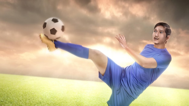 Jugador de fútbol asiático con una camiseta azul pateando la pelota