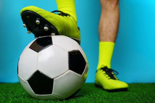 Jugador de fútbol con balón sobre la hierba verde y fondo azul.