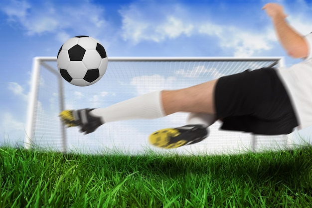 Foto jugador de fútbol de blanco pateando la pelota contra el campo de hierba bajo el cielo azul