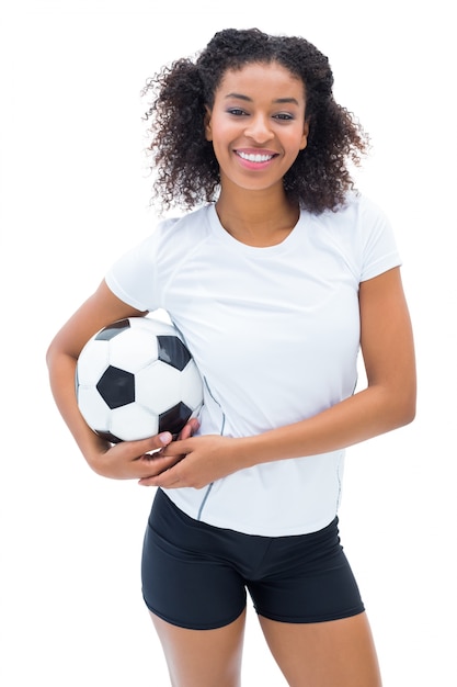 Jugador de fútbol bonito en blanco sosteniendo la bola sonriendo a la cámara