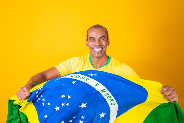 Jugador de fútbol brasileño celebrando con un fondo amarillo Partidario brasileño de hombre afro celebrando sosteniendo la bandera de brasil