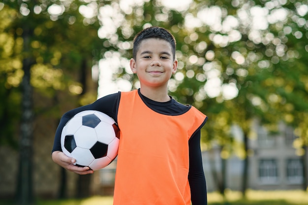 Jugador de fútbol en chaleco naranja sostiene la pelota en una mano después del entrenamiento