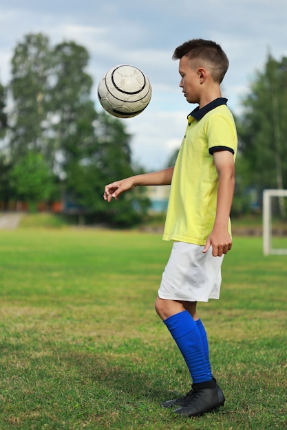 Jugador de fútbol chico guapo con una camiseta amarilla en el campo de fútbol hace malabares con la pelota