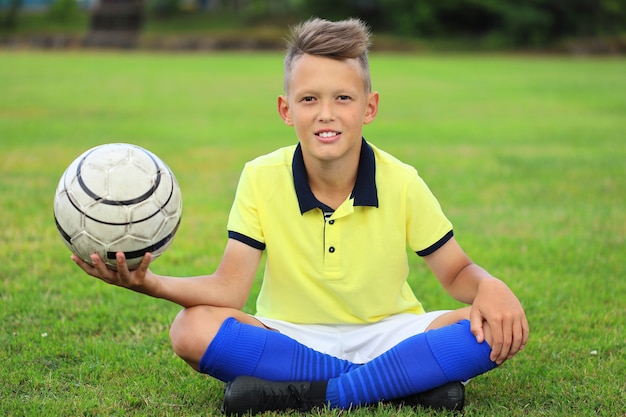 Jugador de fútbol chico guapo sentado en el campo de fútbol