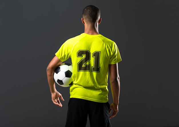 Jugador de fútbol hombre con piel oscura jugando a atrapar una pelota con las manos sobre fondo oscuro