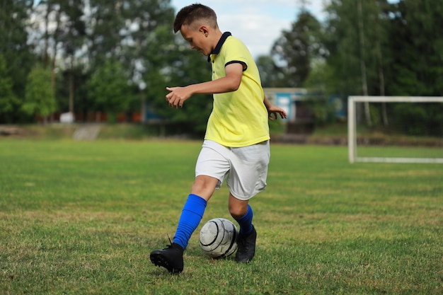 Jugador de fútbol de niño en una camiseta amarilla en el campo de fútbol juega con una pelota