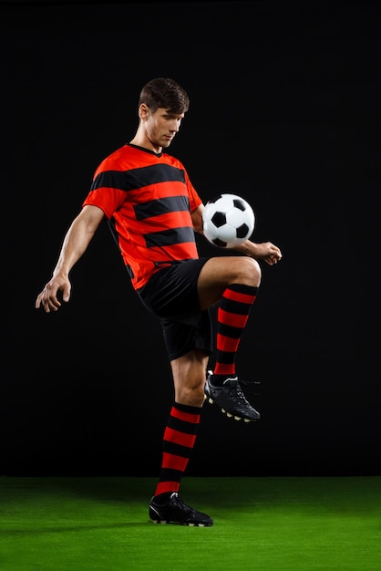 Foto jugador de fútbol, patear, pelota, encima, fondo negro