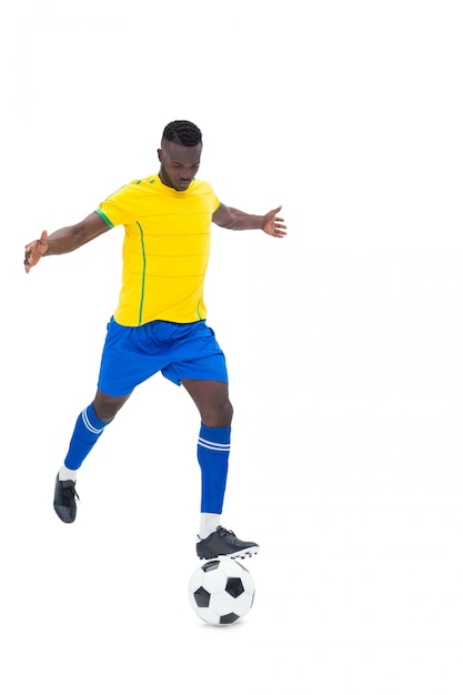 Jugador de fútbol en pelota amarilla pateando sobre fondo blanco