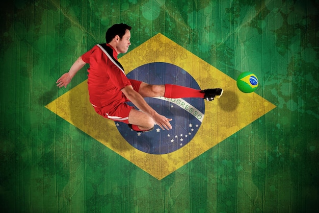Foto jugador de fútbol en rojo pateando contra la bandera de brasil en efecto grunge