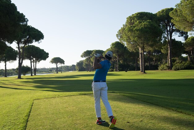 jugador de golf golpeando un tiro con el club en el campo en una hermosa mañana con una llamarada solar en el fondo