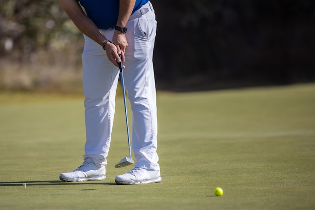 Jugador de golf masculino golpeando la pelota con zapatos blancos