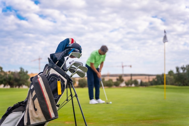 Jugador de golf profesional caucásico en el green preparándose para el tiro al lado de la calle llevando bolsas