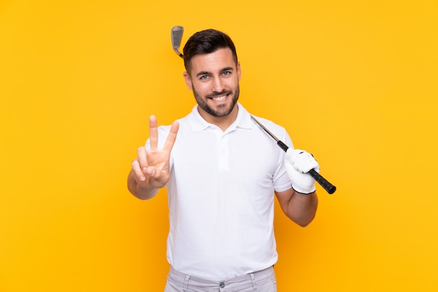 Jugador de golfista hombre sobre pared amarilla aislada sonriendo y mostrando signos de victoria