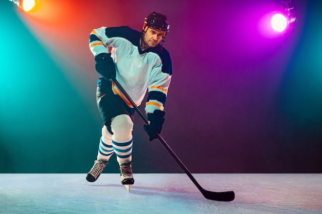 Jugador de hockey masculino en la cancha de hielo y fondo de neón oscuro, deporte