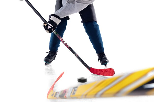 Jugador de hockey masculino irreconocible con el palo en la cancha de hielo y fondo blanco.