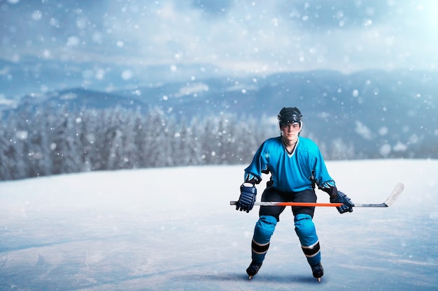 Un jugador de hockey con palo sobre hielo abierto, concepto de juego, bosque nevado. Persona del sexo masculino en casco, guantes y uniforme de protección al aire libre, juego de deportes de invierno