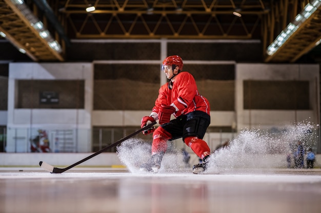 Jugador hokey hermoso caucásico fuerte dedicado que juega al hockey sobre hielo en el pasillo.