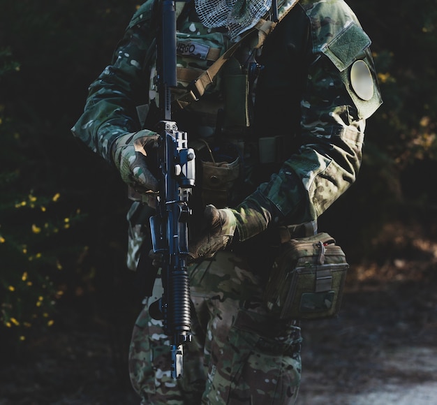 Jugador del juego militar Airsoft en uniforme de camuflaje con rifle de asalto armado.