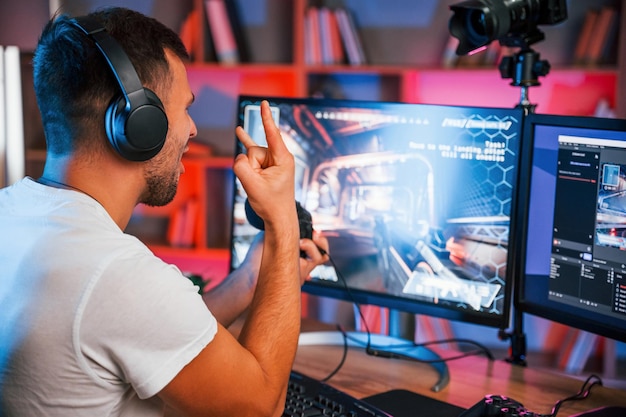 El jugador de juegos masculino en ropa casual está en el interior con la computadora