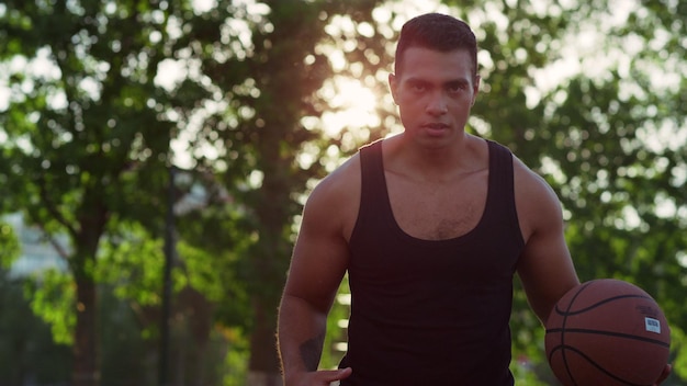 Jugador masculino de streetball musculoso enfocado practicando baloncesto solo al aire libre