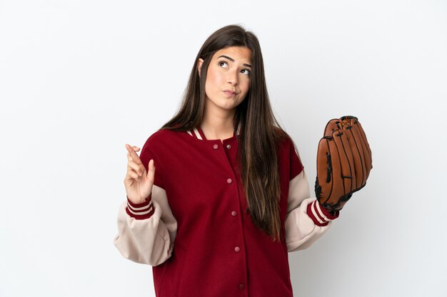 Jugador mujer brasileña con guante de béisbol aislado sobre fondo blanco con los dedos cruzando y deseando lo mejor