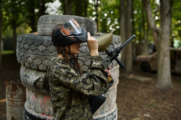 Jugador de paintball femenino con poses de pistola en el patio de recreo en el bosque