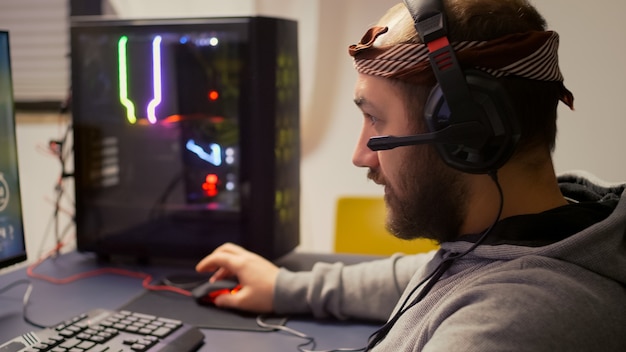 Jugador profesional poniéndose auriculares con micrófono jugando videojuegos de disparos en primera persona en un estudio de juegos en casa. Jugador competitivo que transmite cibernética en línea durante el torneo