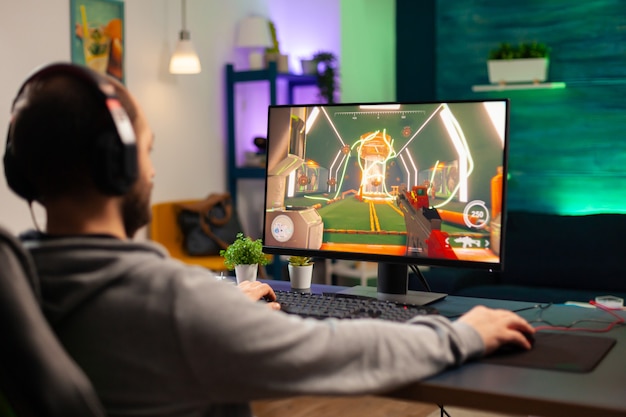 Jugador profesional que juega en videojuegos de computadora para torneos usando auriculares profesionales. Rendimiento cibernético de transmisión en línea durante la competencia de juegos utilizando tecnología de red inalámbrica