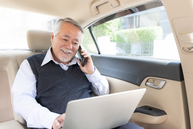 Jugador rico del comerciante de la acción del hombre rico mayor del negocio en el traje que trabaja con la computadora de computadora portátil en su coche