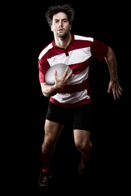 Jugador de rugby en un funcionamiento uniforme rojo. Pared negra