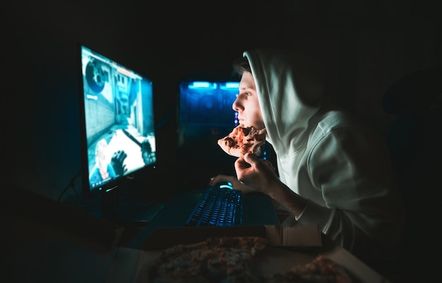 Foto el jugador se sienta en casa en la mesa de la computadora y come pizza