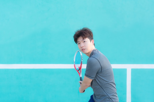 Jugador de tenis asiático joven del hombre que celebra la estafa - retrato del revés.