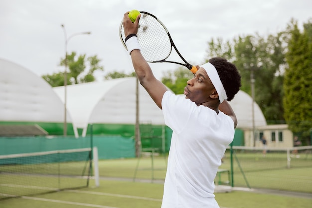 El jugador de tenis está entrenando en la cancha de tenis. El niño sostiene la pelota de tenis y la raqueta en las manos.