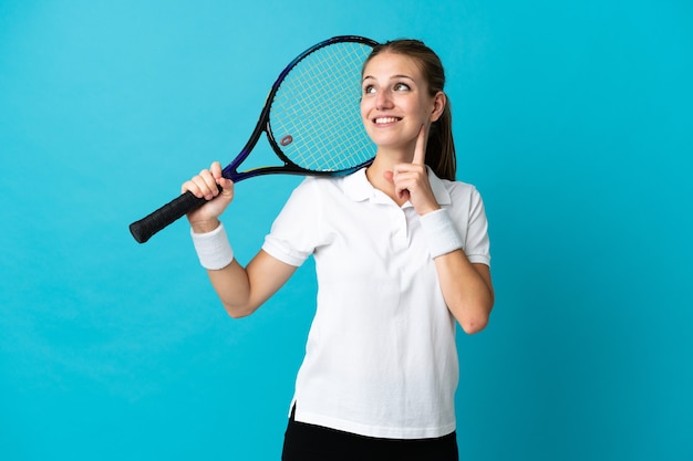 Jugador de tenis joven aislado en la pared azul pensando en una idea mientras mira hacia arriba