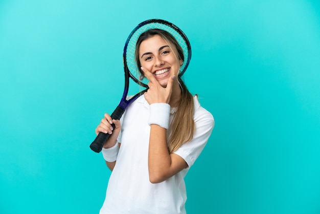 Jugador de tenis joven aislado sobre fondo azul feliz y sonriente