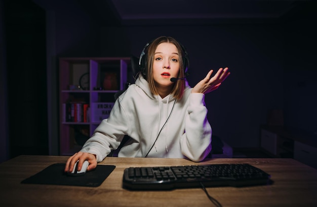 Foto una jugadora sorprendida con ropa casual blanca y auriculares juega juegos de computadora en línea