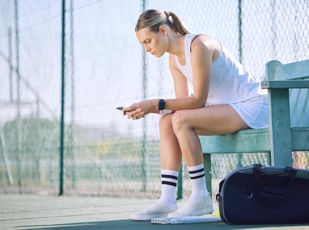 Jugadora de tenis con un teléfono revisando el progreso de la meta de fitness en una aplicación de ejercicio moderna en línea mientras toma un descanso en la cancha Una mujer deportista mirando mensajes en el teléfono celular y esperando al entrenador