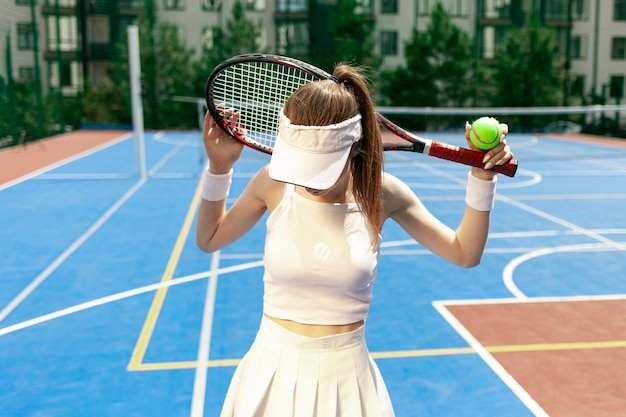 Foto jugadora de tenis con uniforme blanco sosteniendo una raqueta en la cancha de tenis atleta femenina jugando al tenis