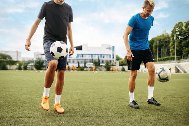 Los jugadores de fútbol masculinos rellenan el balón con los pies en el campo. Futbolistas en el estadio al aire libre, entrenamiento del equipo antes del juego