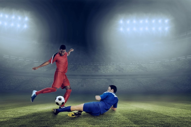 Foto los jugadores de fútbol que abordan el balón contra el gran estadio de fútbol bajo un cielo azul
