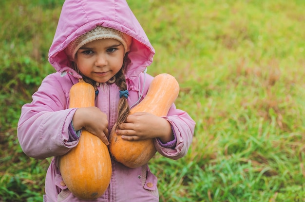 Jugando al aire libre linda niña sosteniendo una calabaza. Cosecha de calabazas, otoño en el jardín, la niña encantadora y calabazas grandes.