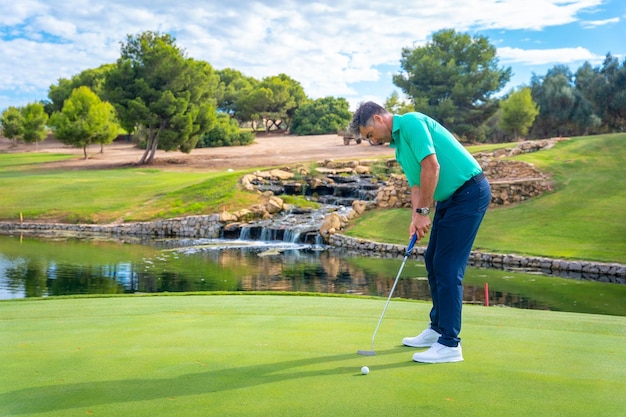 Jugando al golf en el club de golf junto a un lago en el green golpeando la pelota con el putter