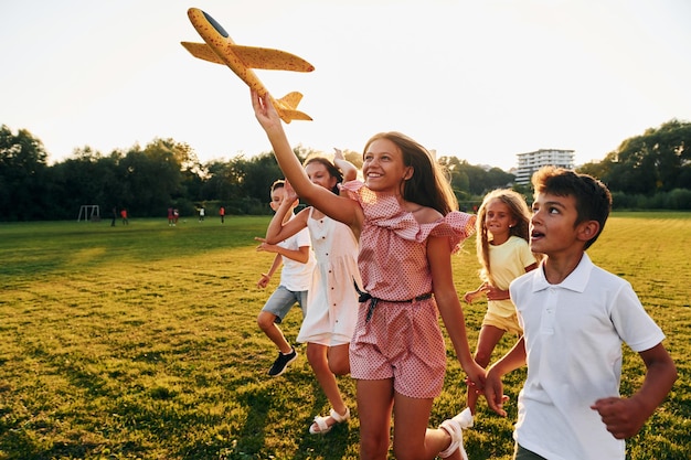 Jugando con un avión de juguete Grupo de niños felices está al aire libre en el campo deportivo durante el día