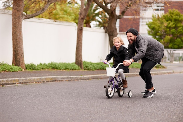 Jugando y creciendo juntos Fotografía de un padre enseñando a su hijita a andar en bicicleta