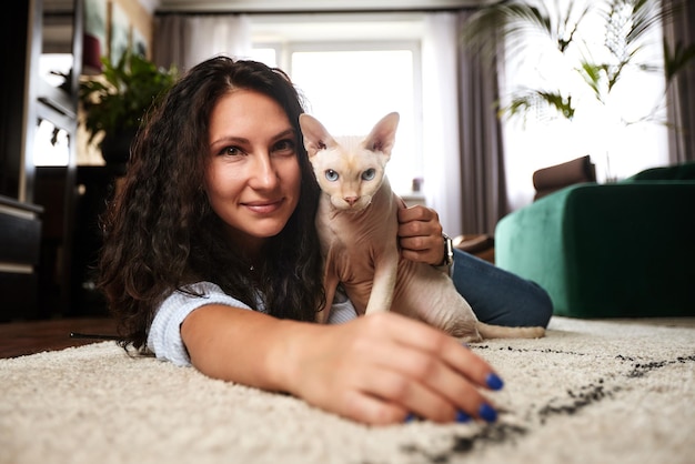 Jugando con gato en casa Mujer joven tirada en el suelo y abrazando mascota